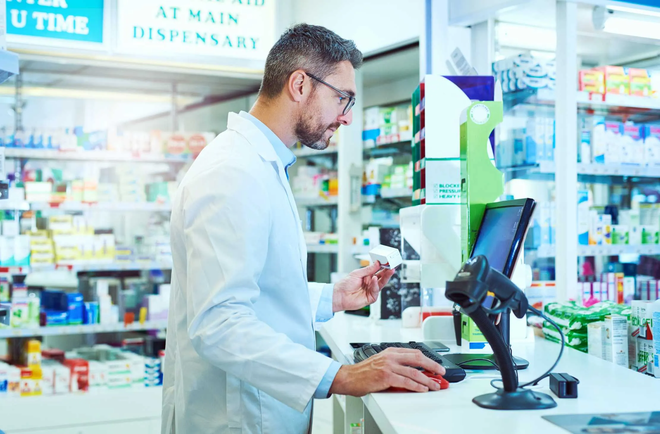 Pharmacist at the dispensary computer recording a prescription sale tied to a specific medicine batch