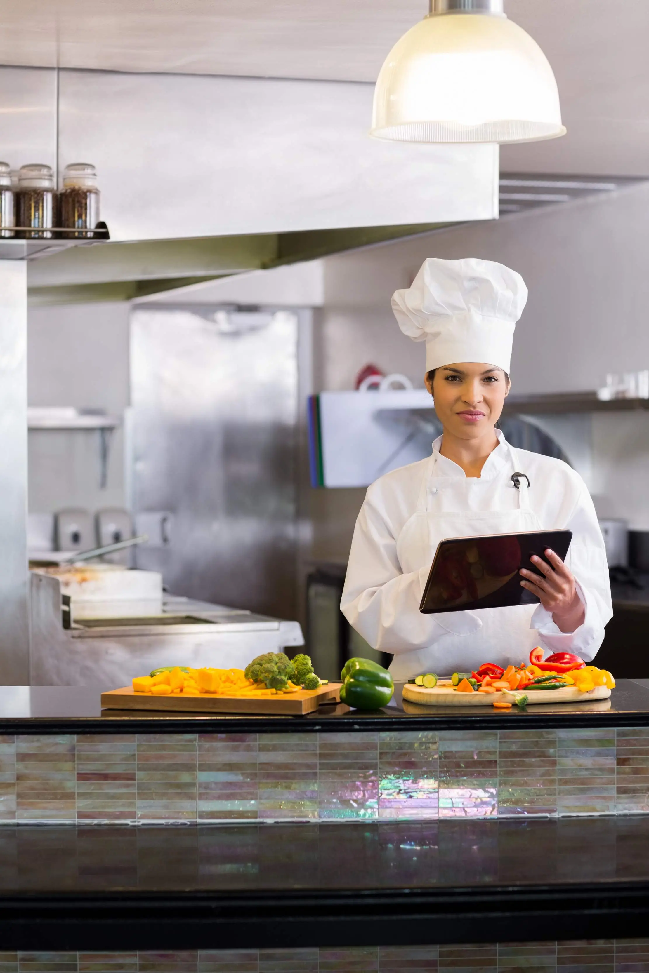 Cheffe tenant une tablette à côté de légumes préparés dans une cuisine professionnelle